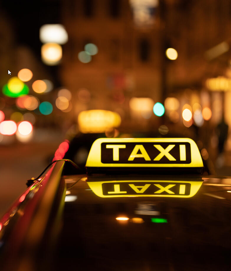 Taxi Rank A taxi sign lit up on a car roof at night. the photo background is of a cityscape but its blurred out and the focus of the photo is the taxi sign